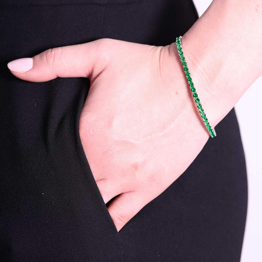 Braccialetto a tennis con smeraldi al polso di una donna, che tiene la mano in tasca.