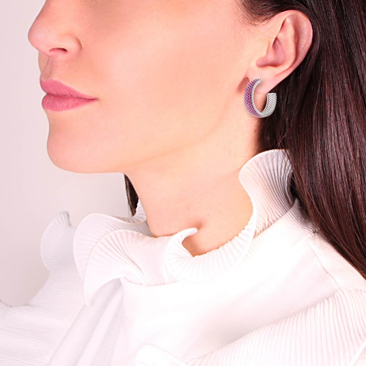 Orecchini a cerchio bicolore, metà rosa e metà argento, indossati da una donna con capelli scuri e una camicia bianca.
