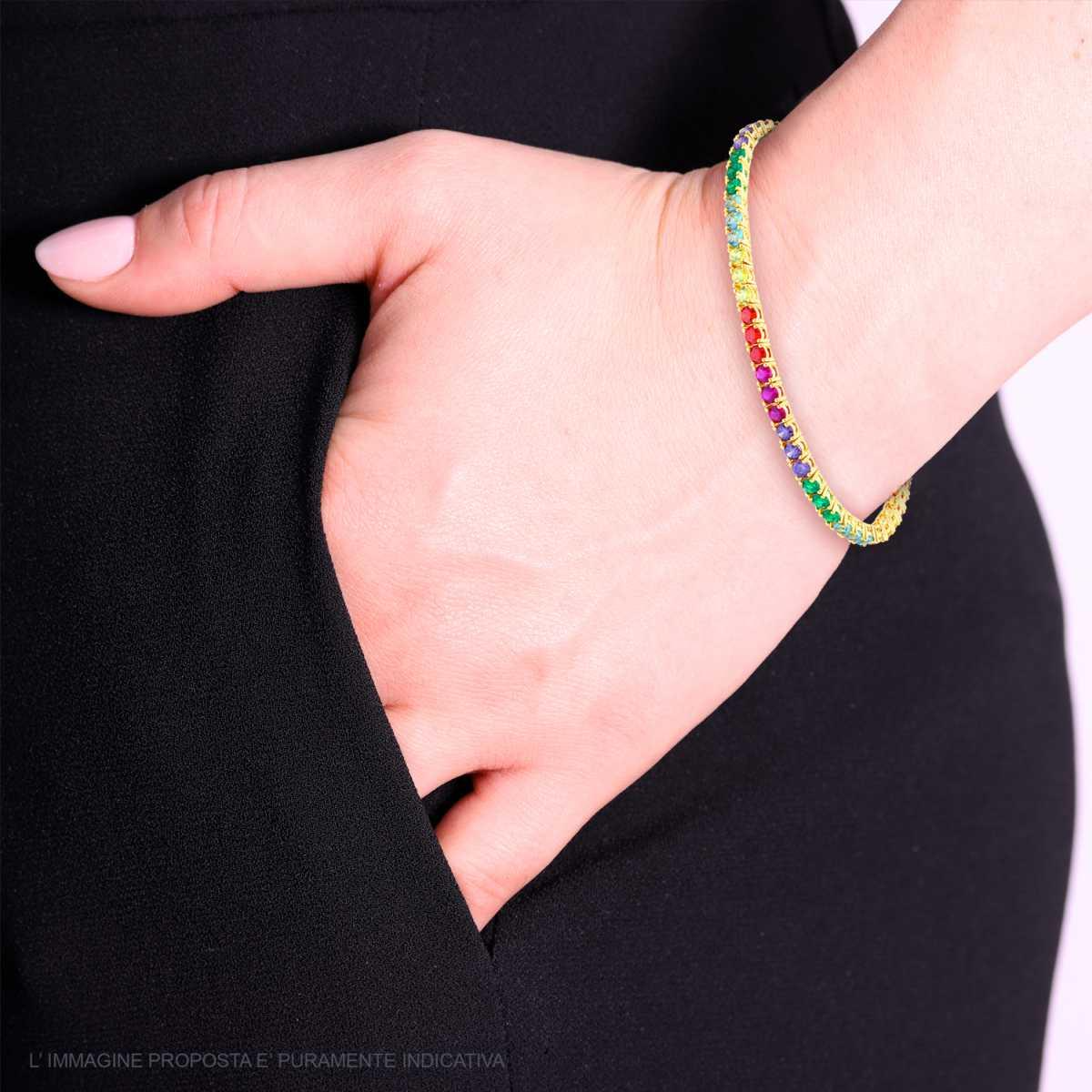 Bracciale tennis con zirconi colorati, indossato su una mano che poggia su un pantalone nero.