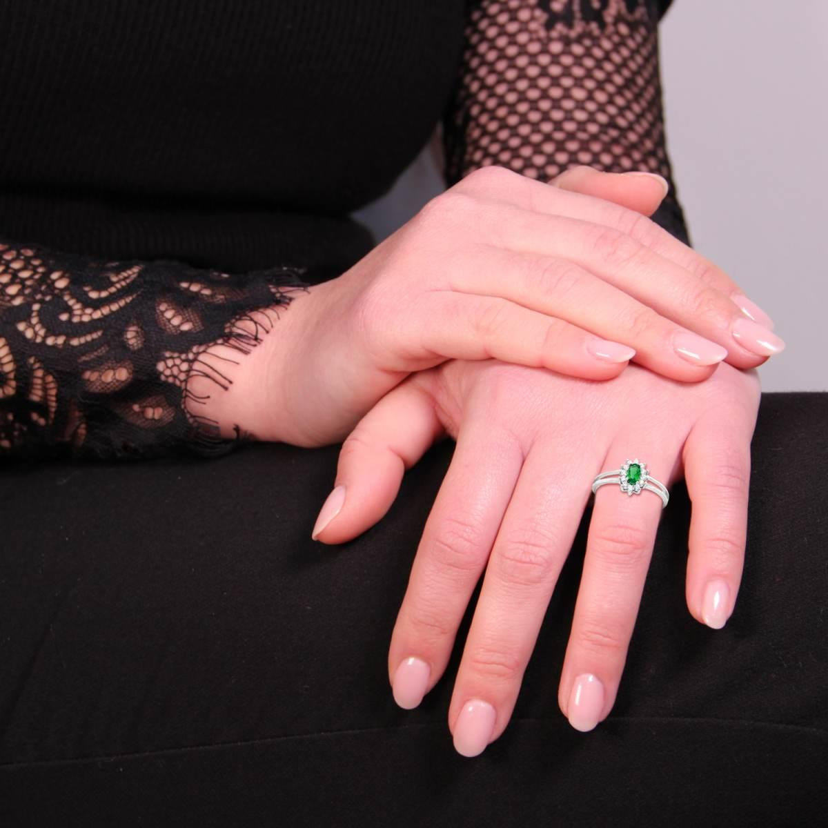 Anello con smeraldo ovale e contorno di diamanti, indossato sulla mano di una donna.
