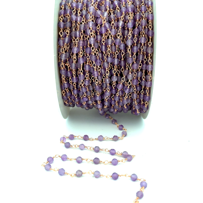Catena di ametiste viola su filo d'oro, avvolta su una bobina, con un pezzo srotolato.