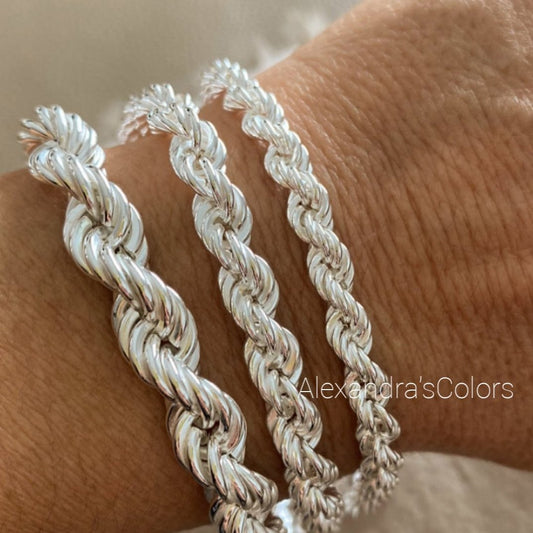 Tre bracciali a corda d'argento di diverse dimensioni indossati su un polso.