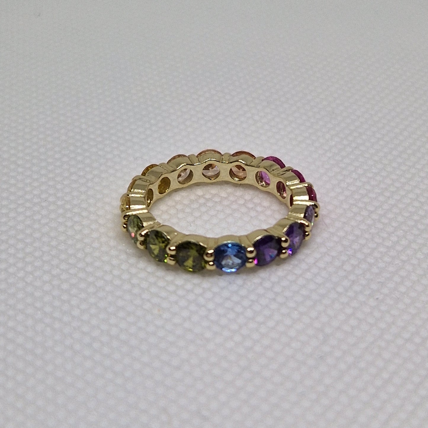 Anello a fascia dorata con pietre preziose multicolori incastonate a giro, su sfondo bianco.