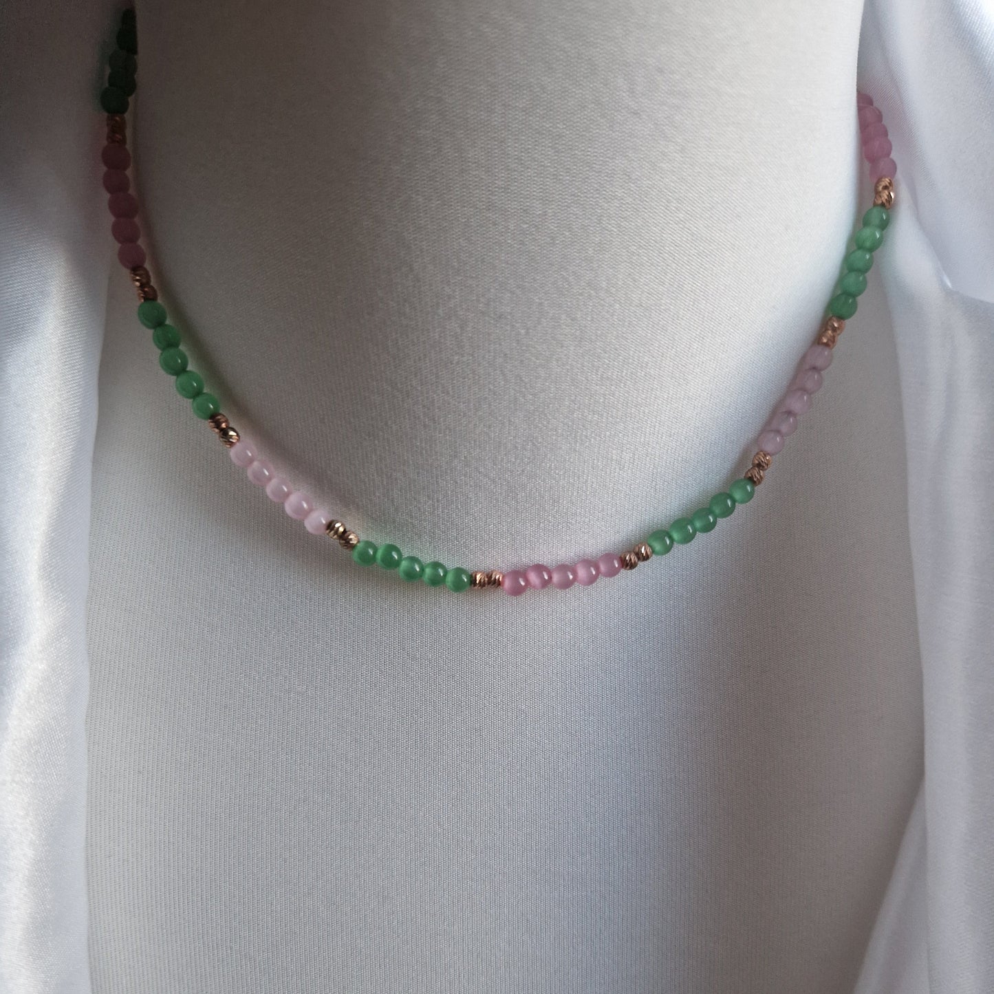 Collana di perline bicolore verde e rosa, con dettagli in metallo color rame, esposta su un manichino.