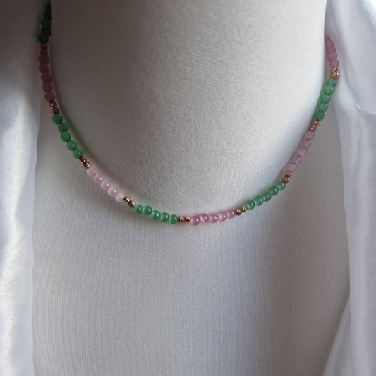 Collana di perline bicolore verde e rosa, con dettagli in metallo color rame, esposta su un manichino.