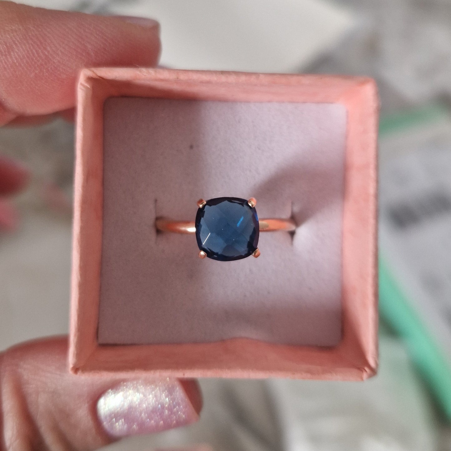 Anello in oro rosa con gemma blu scuro in una scatolina rosa.