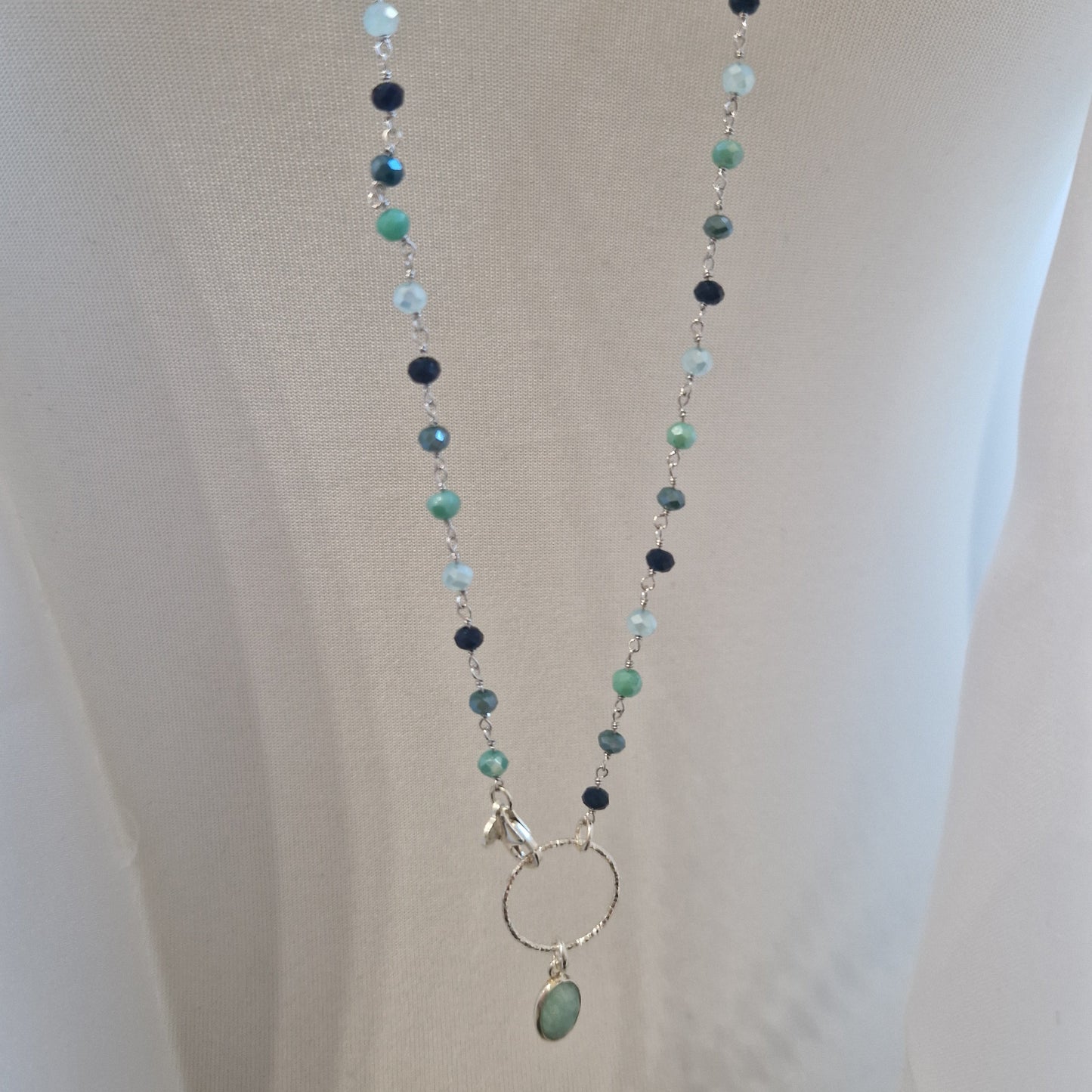 Collana lunga con perline in diverse tonalità di verde e azzurro, con anello e ciondolo a goccia.