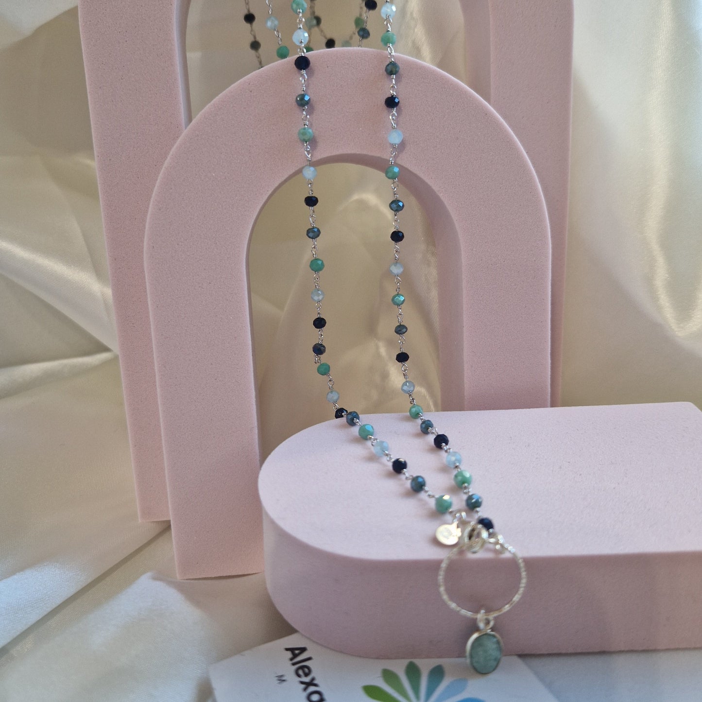 Collana lunga con perline in diverse tonalità di verde e azzurro e ciondolo con anello e pietra verde acquamarina.