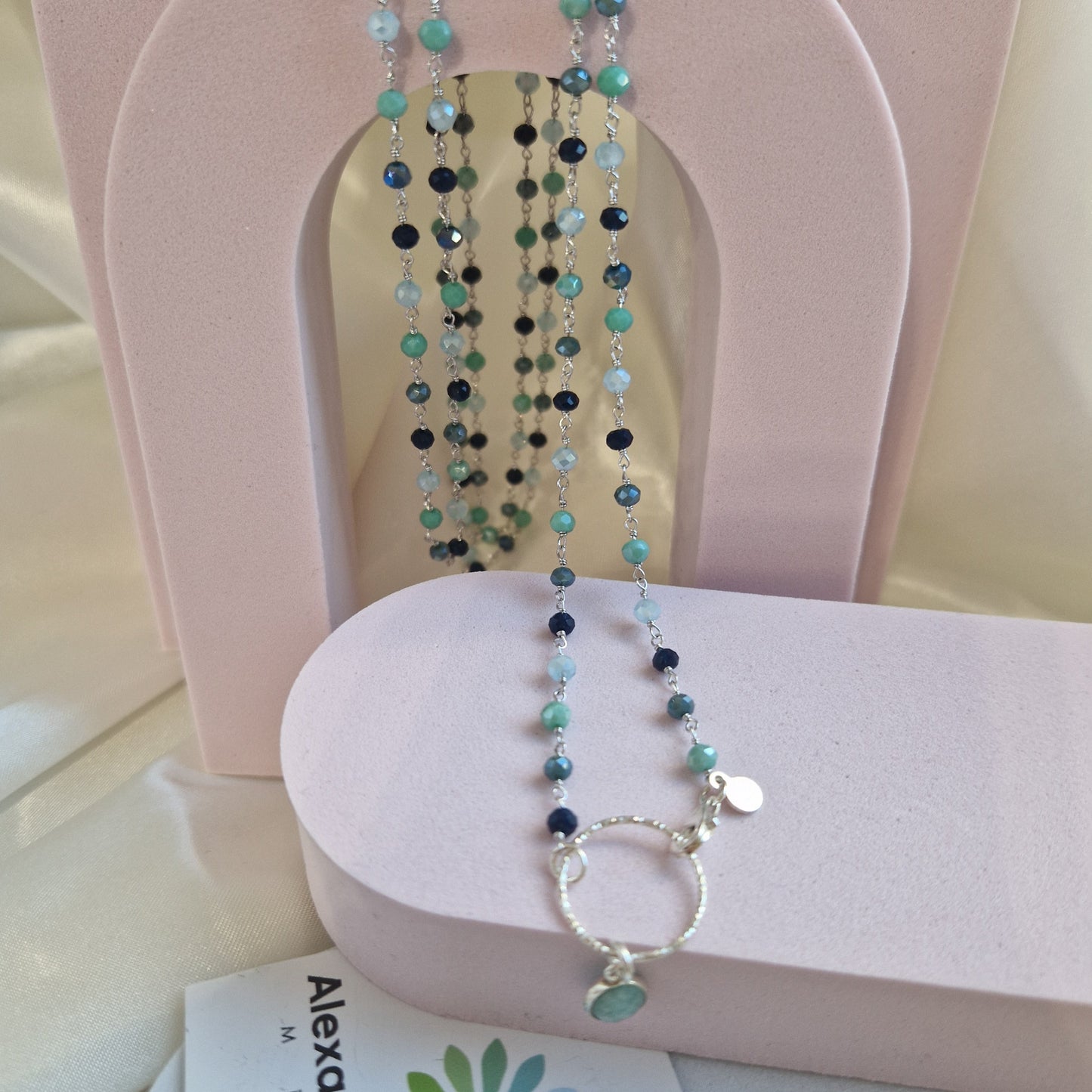 Collana lunga di perline blu, verdi e nere su un manichino con camicetta di seta.
