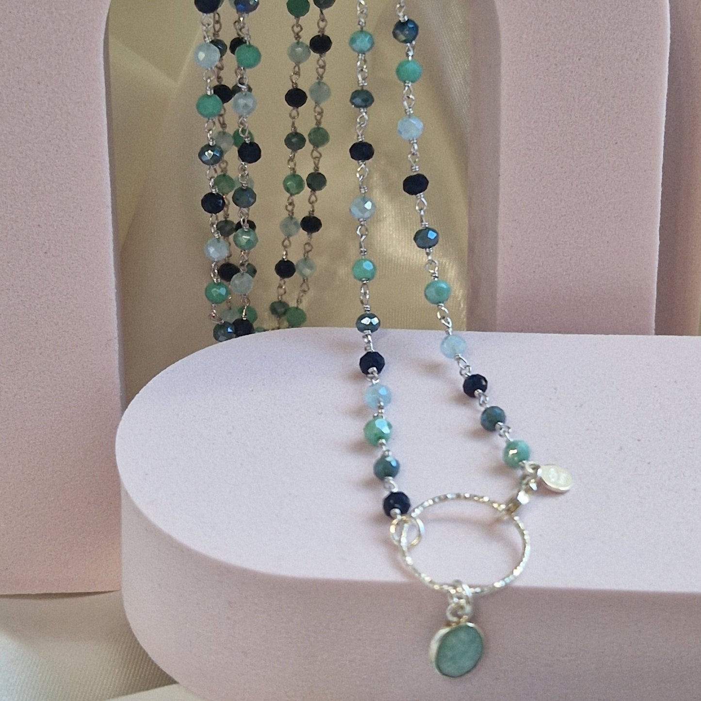 Collana artigianale di perle sfaccettate in tonalità blu e verde con ciondolo a cerchio e pietra verde.