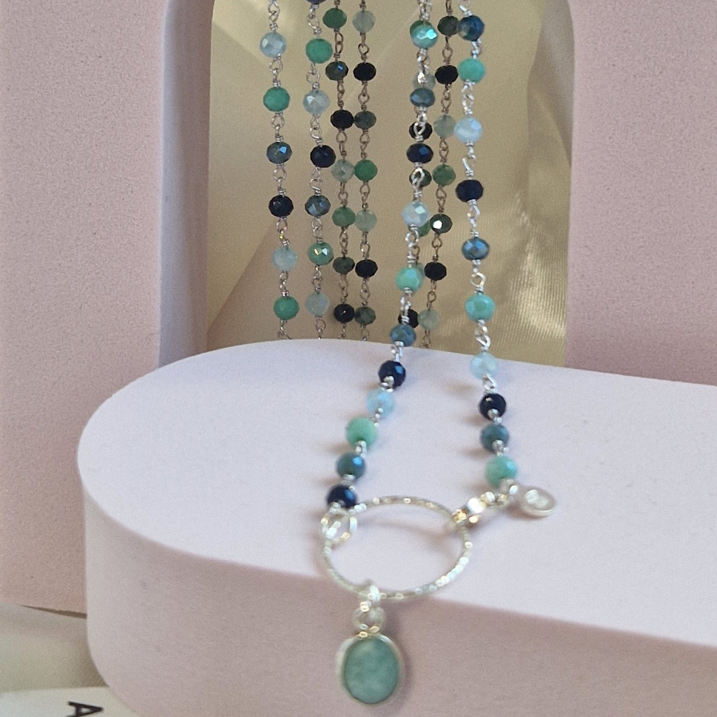 Collana lunga di perline di pietre semipreziose in verde e blu, con chiusura a cerchio d'argento e un ciondolo.