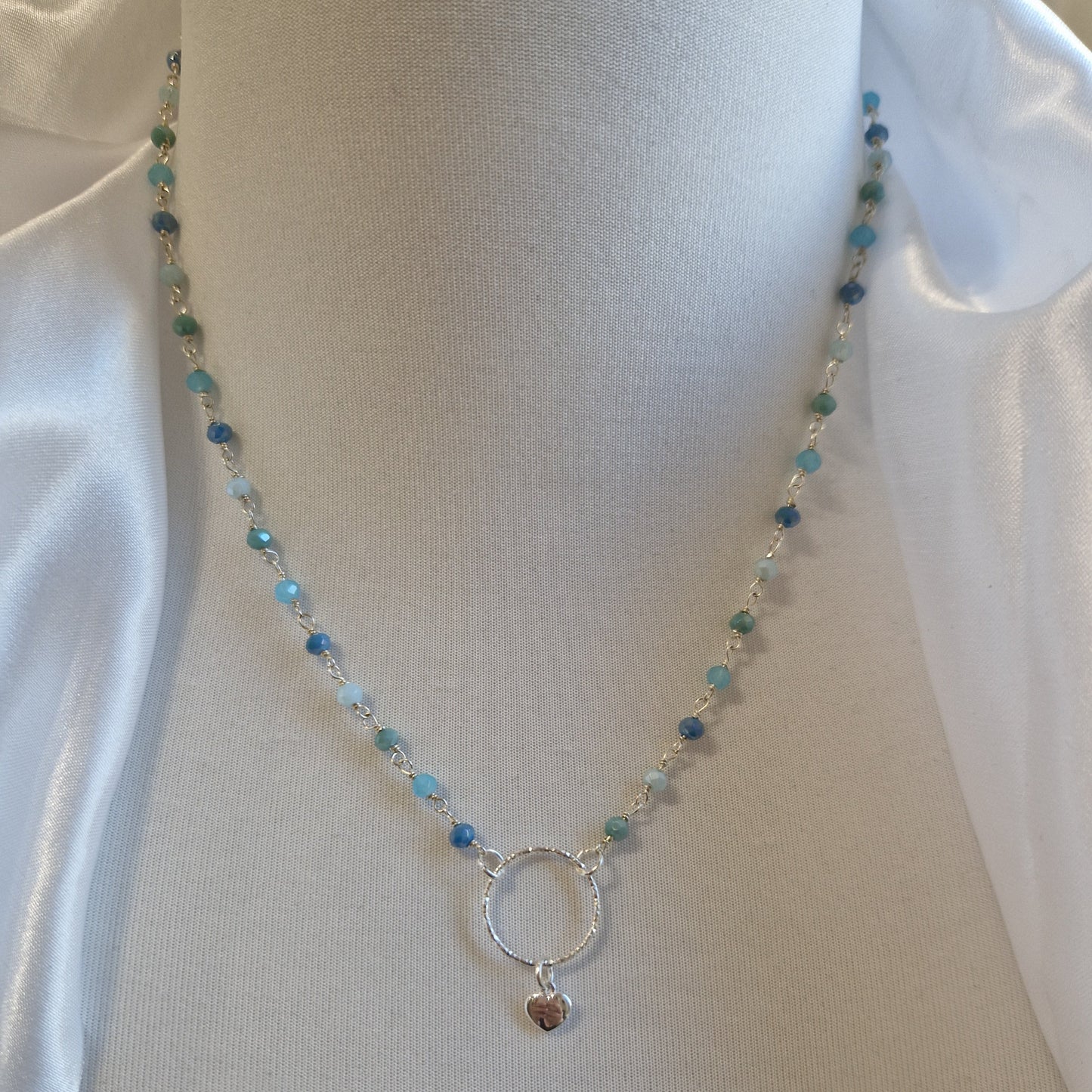 Collana in argento con perline blu e verdi e ciondolo a cerchio con piccolo cuore.