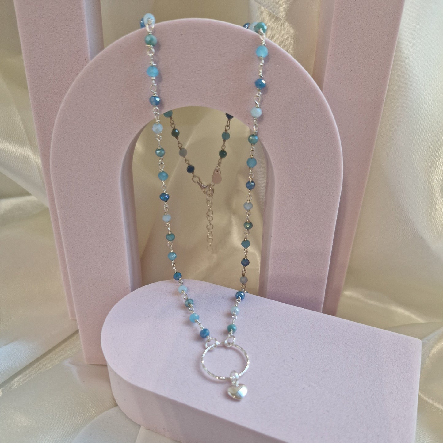 Collana artigianale con perle turchesi e blu, un ciondolo a cerchio in argento e un piccolo cuore.