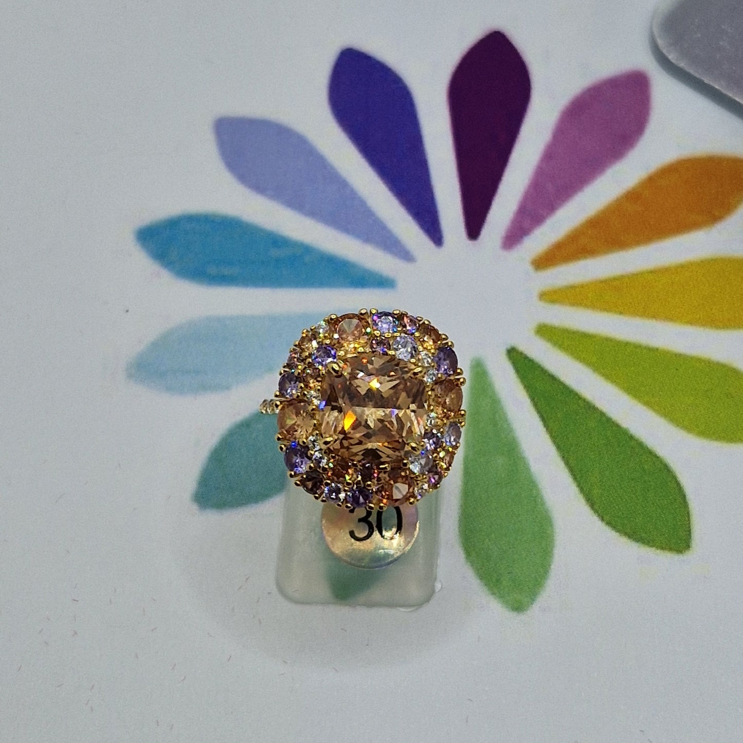 Anello in oro con pietra centrale ovale color pesca circondata da pietre viola e arancioni.