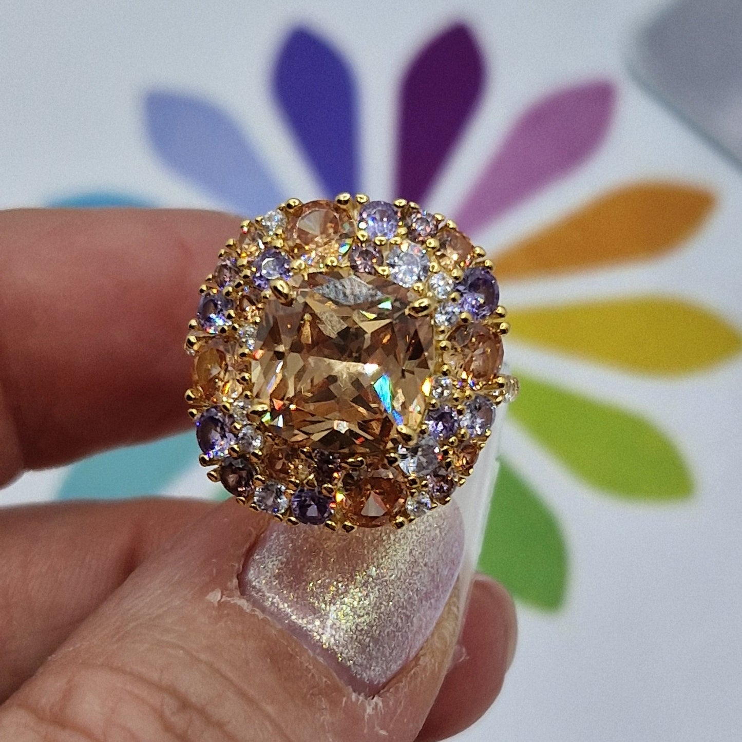 Anello in oro con grande gemma centrale color champagne circondata da pietre più piccole, viola, arancioni e bianche.
