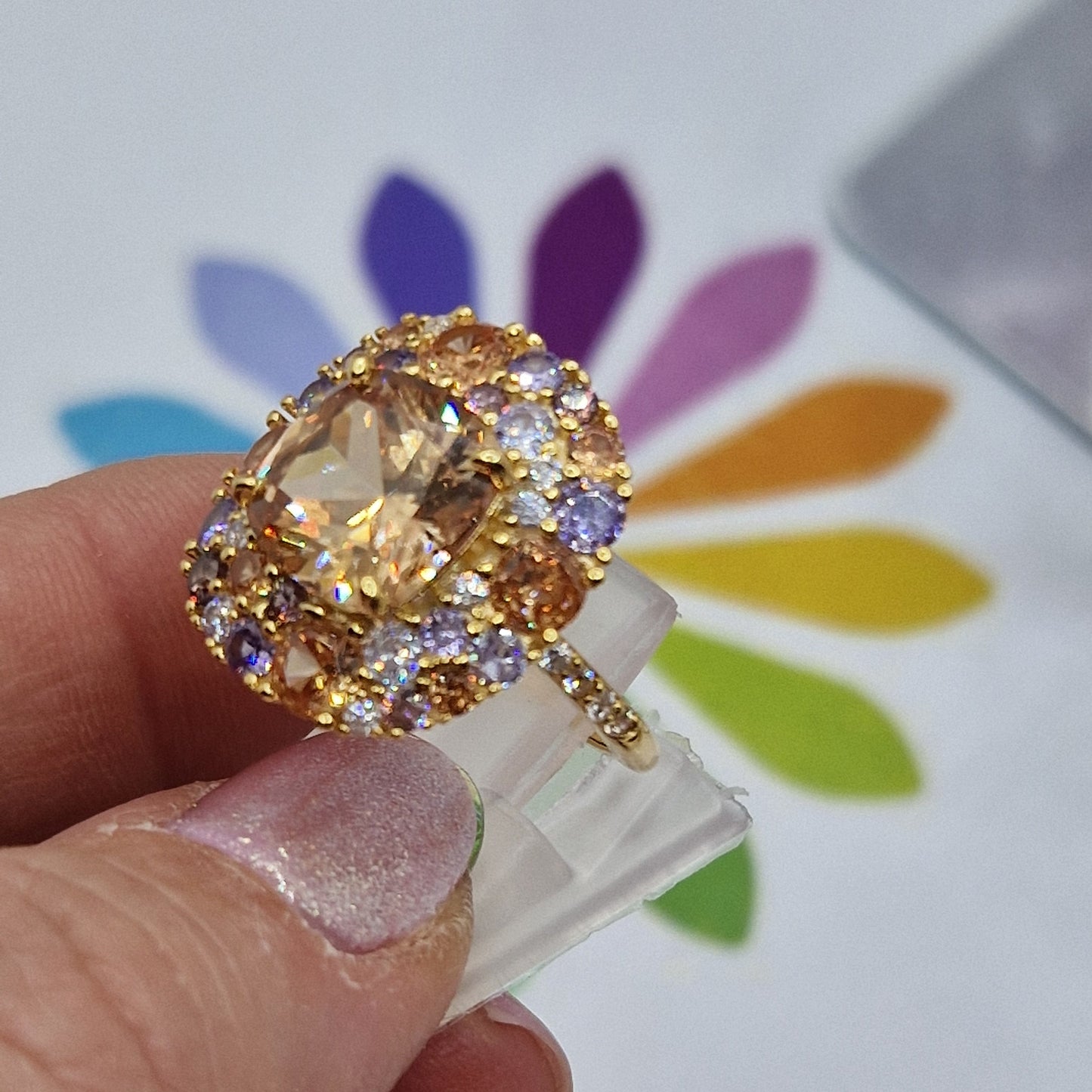 Anello in oro con grande pietra centrale color champagne circondata da pietre viola, arancioni e bianche.
