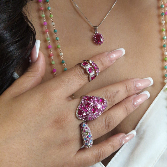 Collana, ciondolo e anelli in argento con pietre preziose rosse e multicolori, su una mano con unghie lunghe.