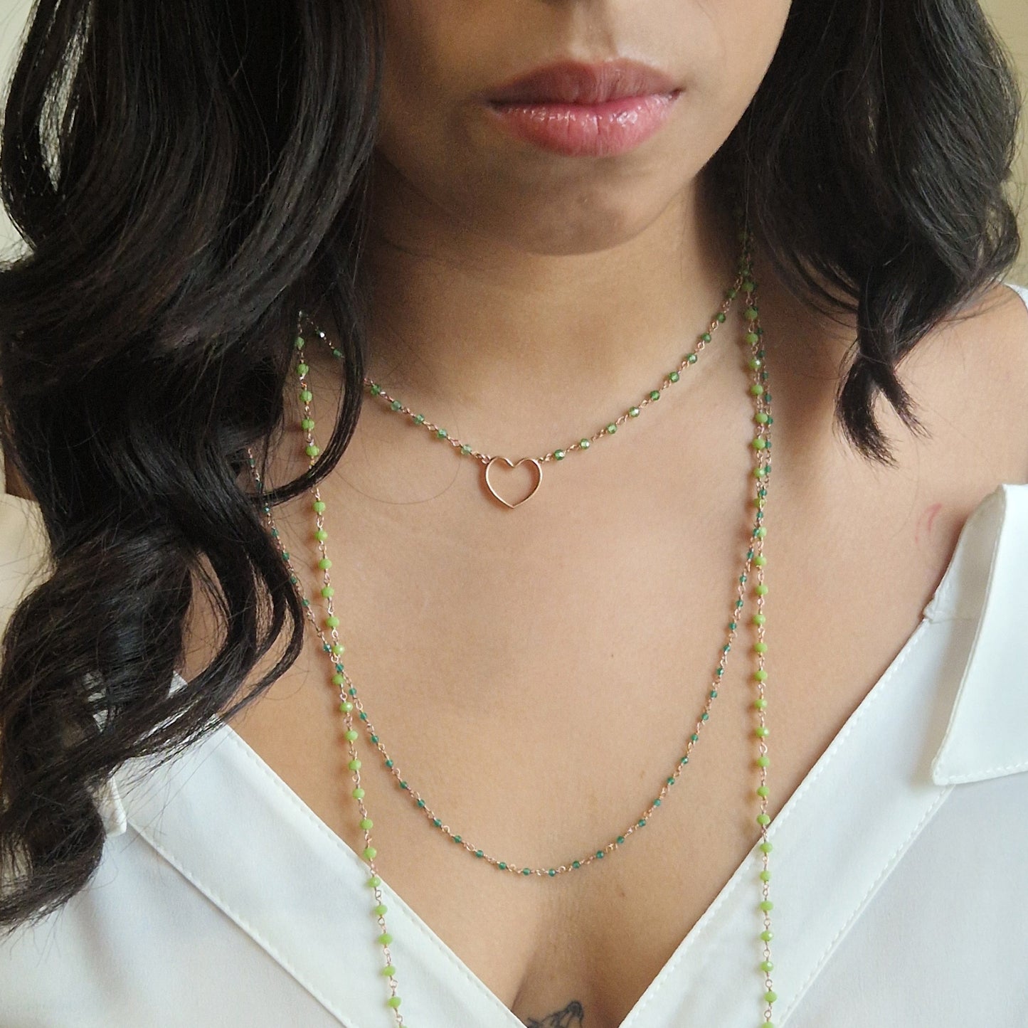 Donna indossa una collana a cuore color oro rosa e una collana lunga con perline verdi.