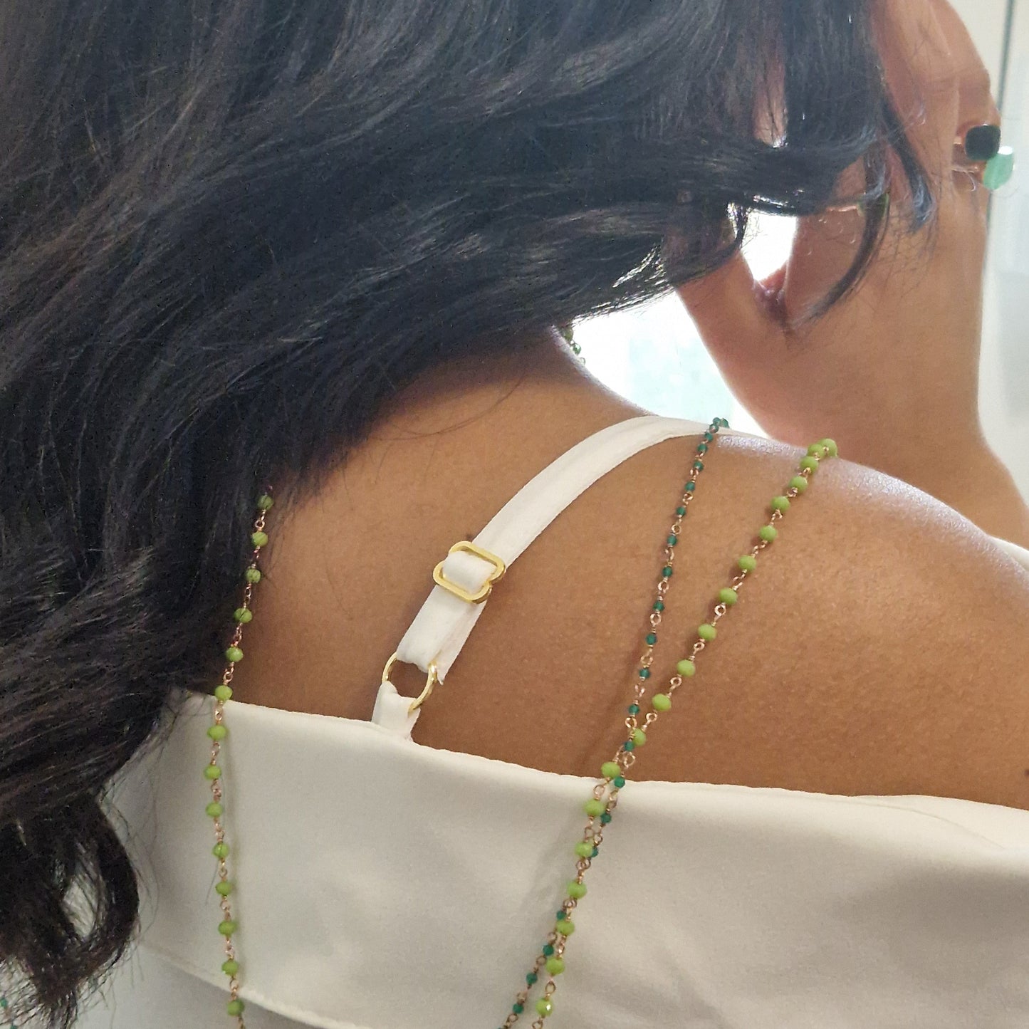 Donna di schiena con spallina bianca e collana di perle verdi, anelli e capelli scuri.