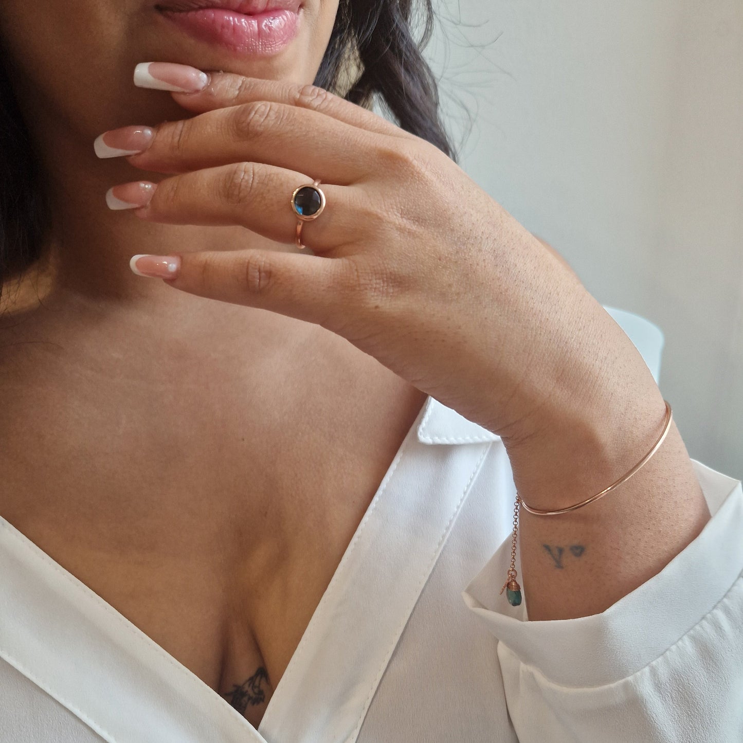 Donna indossa anello con pietra scura e un bracciale sottile. Le sue unghie sono lunghe con french manicure.