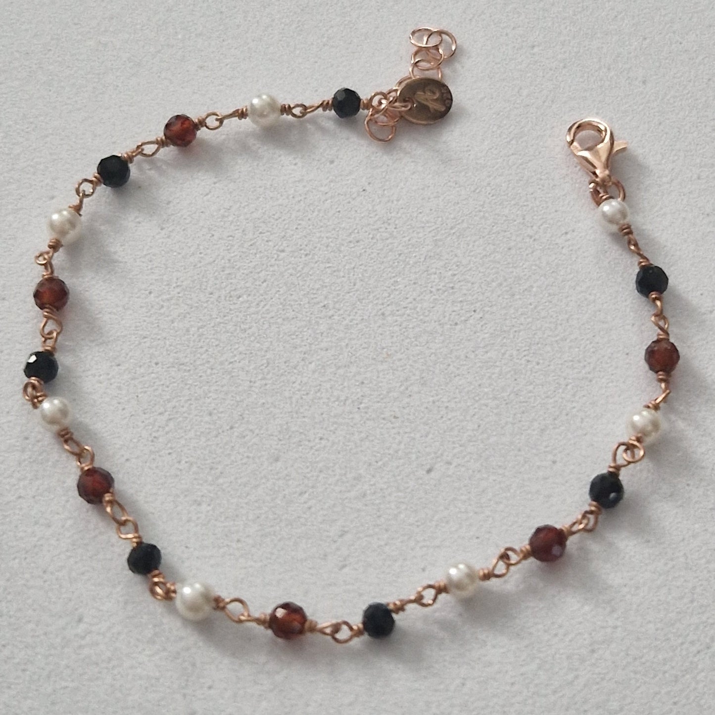Braccialetto artigianale con perle bianche, perle nere e perle marroni sfaccettate su catenina color oro rosa.