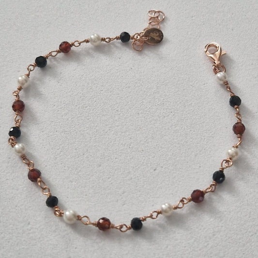 Braccialetto artigianale con perle bianche, perle nere e perle marroni sfaccettate su catenina color oro rosa.