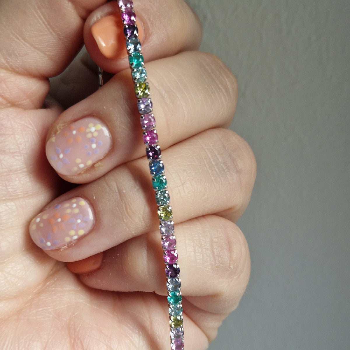Braccialetto a tennis con pietre preziose multicolori, tenuto da una mano con unghie decorate.