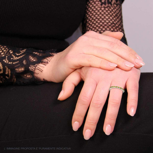 Donna indossa anello eternity con peridoti e diamanti su una mano, l'altra è appoggiata sopra. Abbigliamento nero elegante.