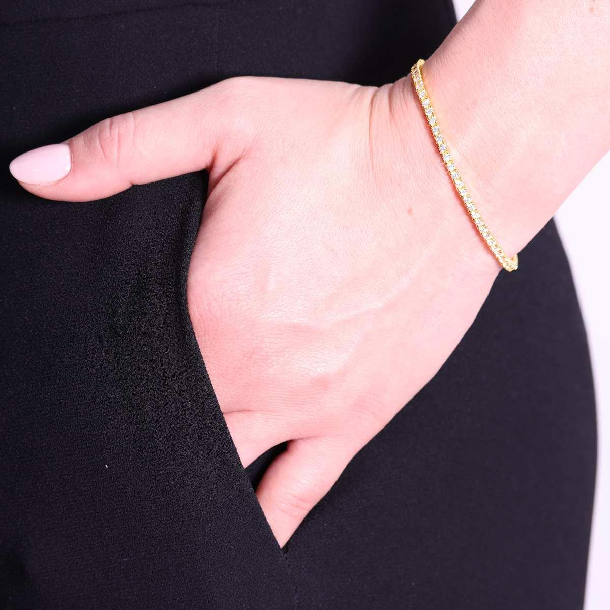 Braccialetto sottile in oro e diamanti su un polso, con una mano nella tasca di un vestito nero.