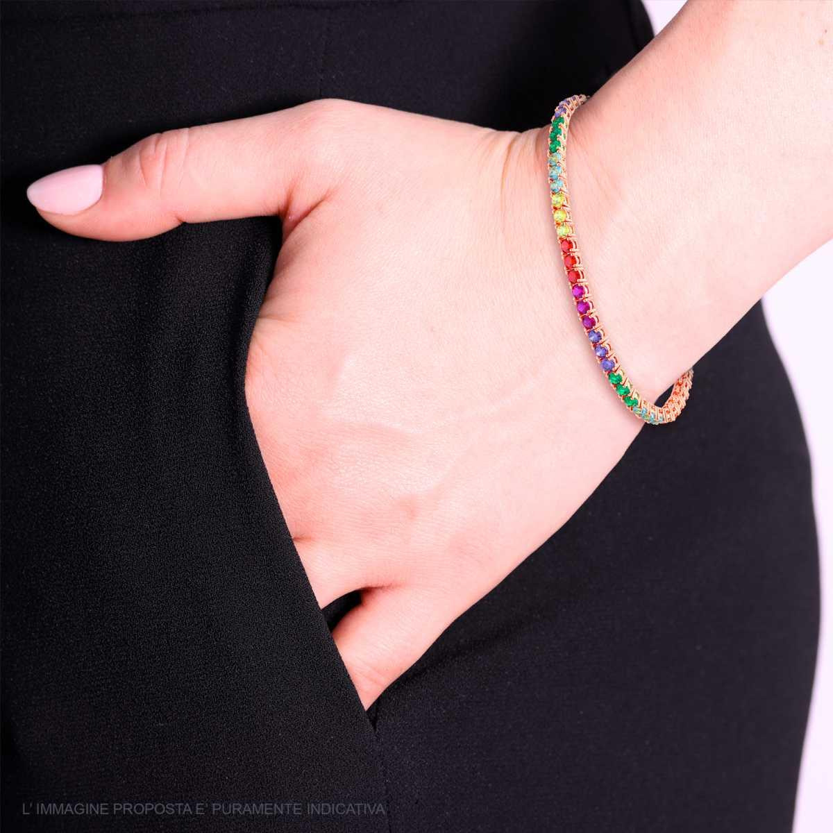 Bracciale tennis in oro rosa con zirconi colorati, indossato al polso di una donna con pantaloni neri.