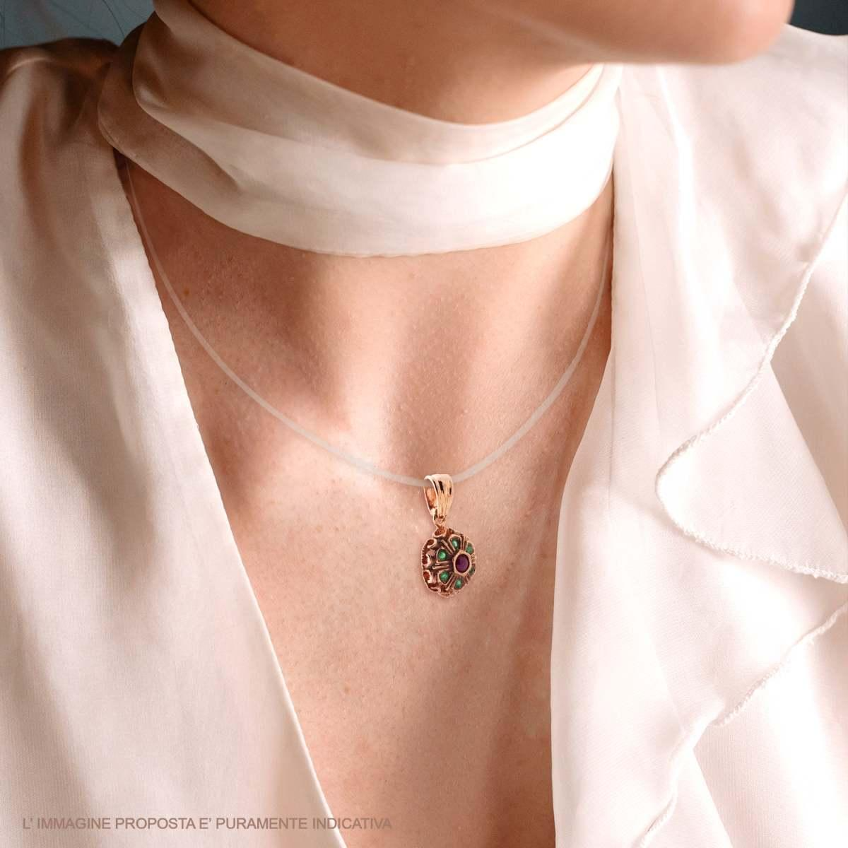Ciondolo a forma di fiore in oro rosa con rubini e smeraldi, indossato su una collana trasparente.