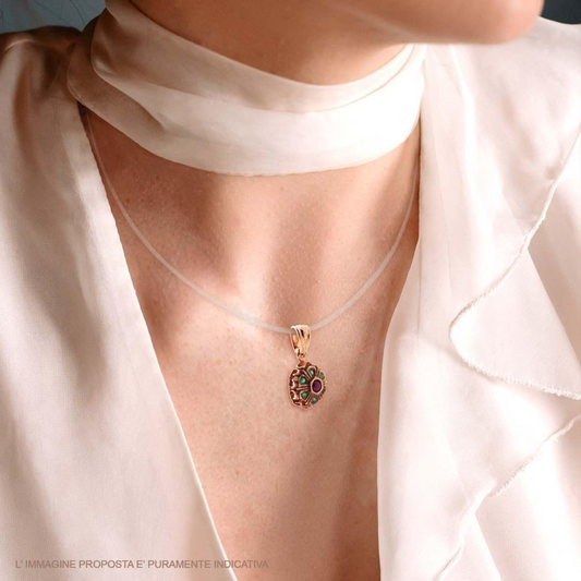 Ciondolo a forma di fiore in oro rosa con rubini e smeraldi, indossato su una collana trasparente.