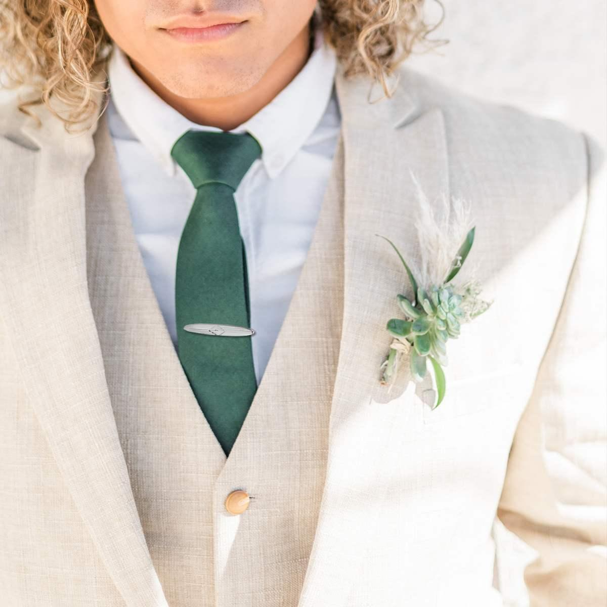 Ritratto di un uomo che indossa un completo da matrimonio color crema con cravatta verde e una bottoniera con succulente e piume.