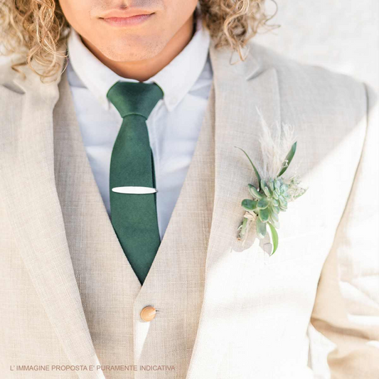 Ritratto di un uomo che indossa un completo da matrimonio color crema con cravatta verde e una bottoniera con succulente e piume.