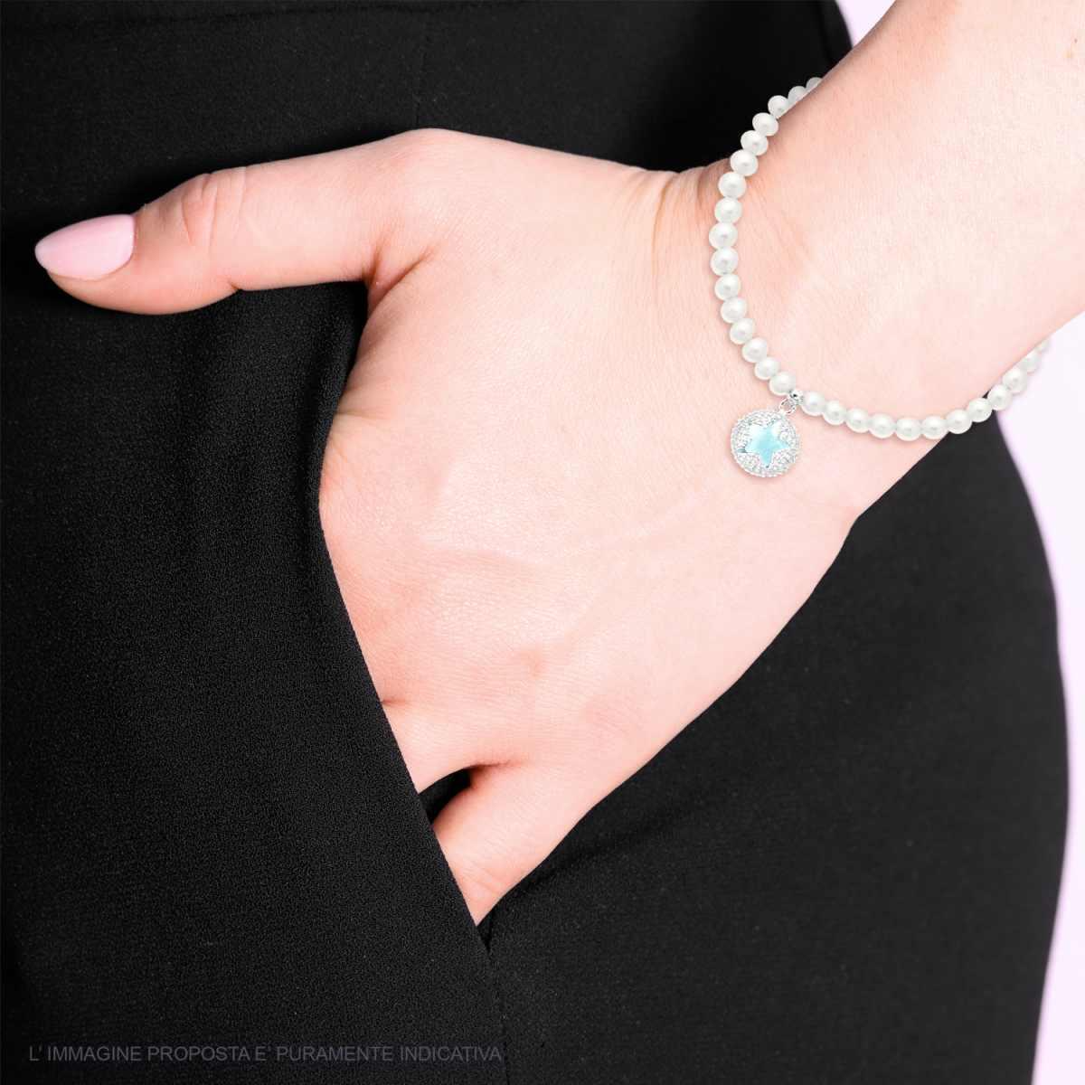 Bracciale di perle con ciondolo in oro bianco e acquamarina, indossato da una donna con pantaloni neri.