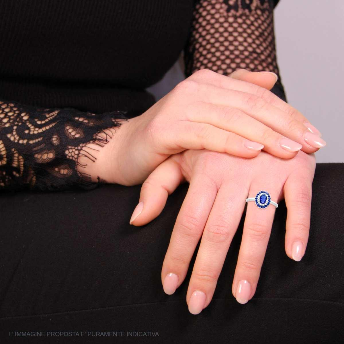 Anello in oro bianco con zaffiro blu centrale e diamanti a contorno su una mano di donna.