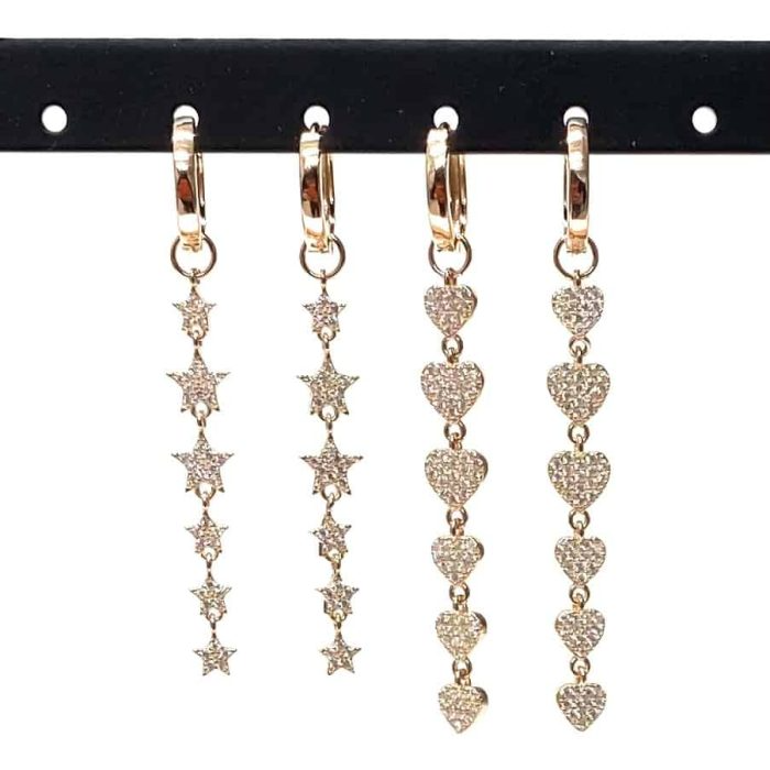 Orecchini pendenti in oro con stelle e cuori, incastonati con piccole gemme scintillanti, esposti su un supporto nero.