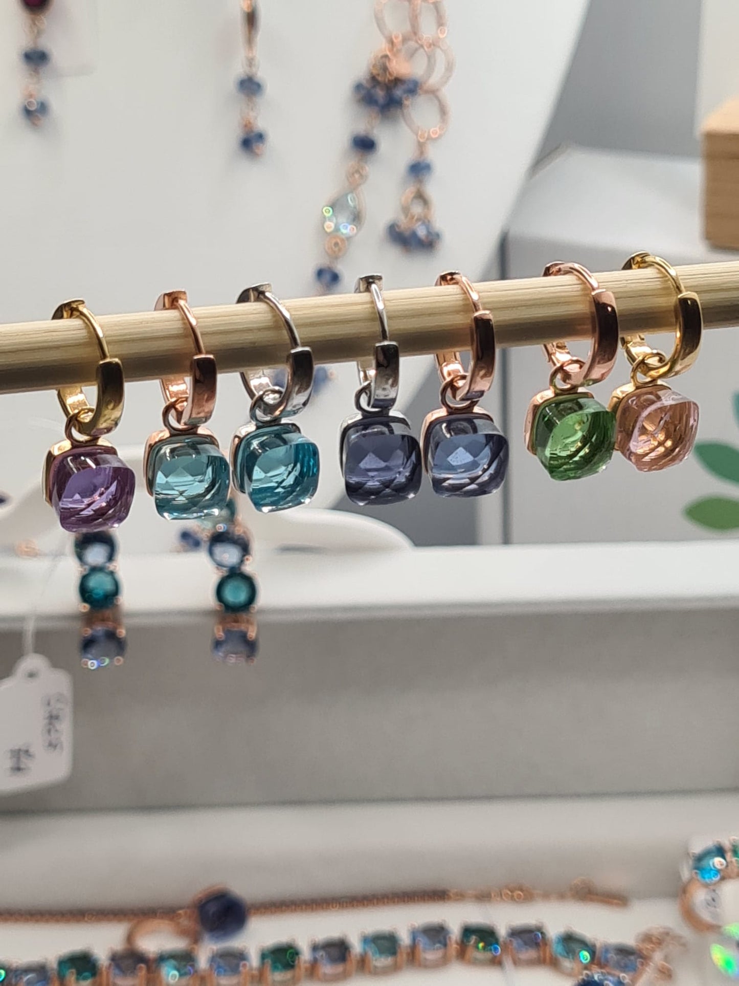 Orecchini pendenti con cristalli quadrati colorati, su supporto di legno.