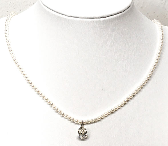 Collana di perle con ciondolo a goccia tempestato di diamanti su un manichino da esposizione bianco.
