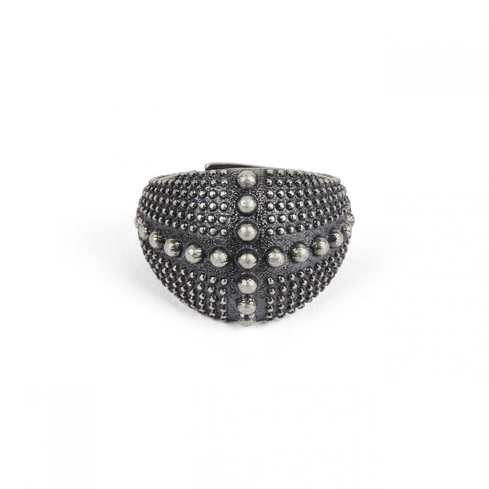 Anello scuro a fascia larga, con una texture a piccole sfere e un motivo a croce di sfere più grandi.