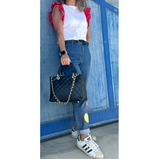 Donna con top bianco e maniche rosse, jeans, borsa nera trapuntata a spalla e sneakers.