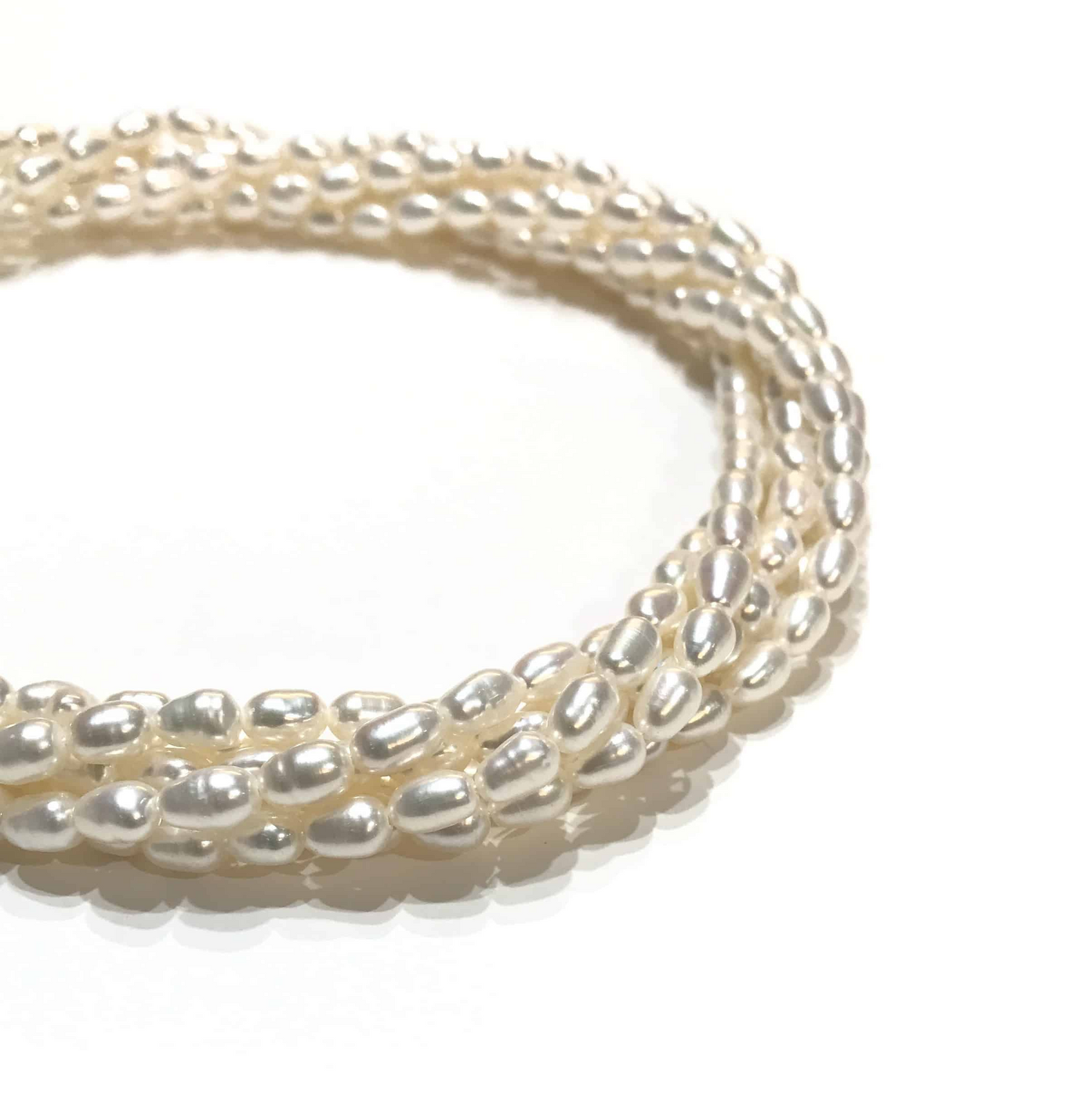 Un primo piano di una collana a più fili di perle d'acqua dolce irregolari, su uno sfondo bianco.