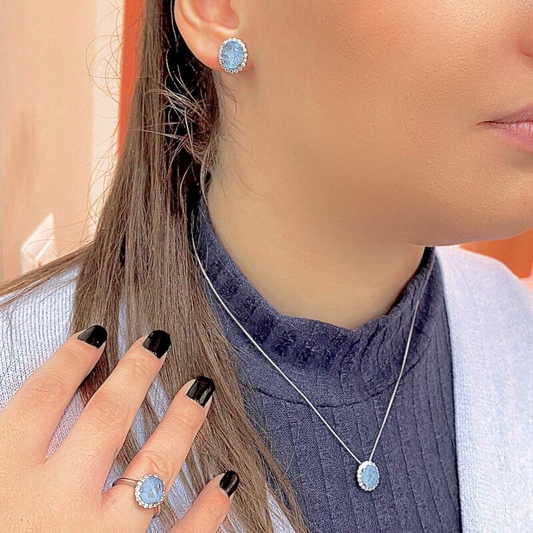 Donna indossa gioielli: anello, orecchini e collana con pietre celesti ovali e dettagli luccicanti.
