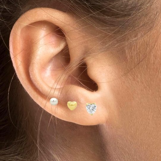 Un orecchio con tre orecchini: una perla, un cuore d'oro e un cuore di diamante.