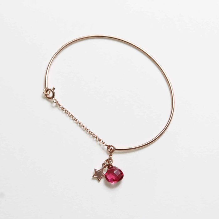 Braccialetto rigido color oro rosa con chiusura a catena e due ciondoli: una stella e una gemma rosa sfaccettata.