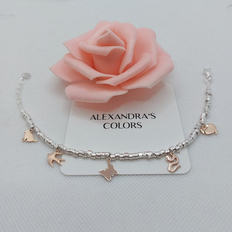 Braccialetto con perline d'argento e ciondoli a forma di animali e farfalle in oro rosa, su sfondo bianco con una rosa.