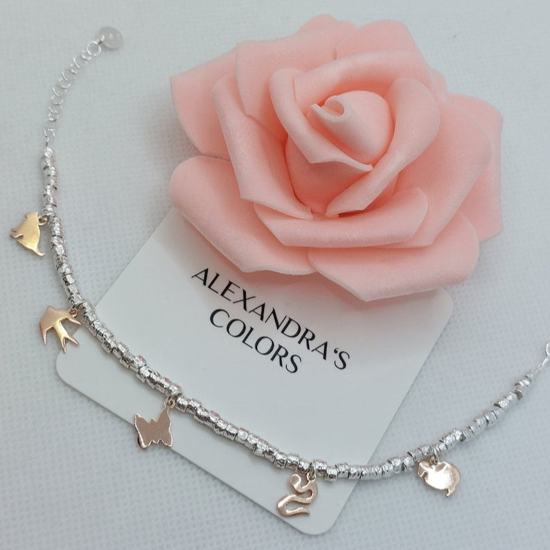 Catenina alla caviglia con perline d'argento e 5 ciondoli a forma di animali, su una carta con scritta "ALEXANDRA'S COLORS".