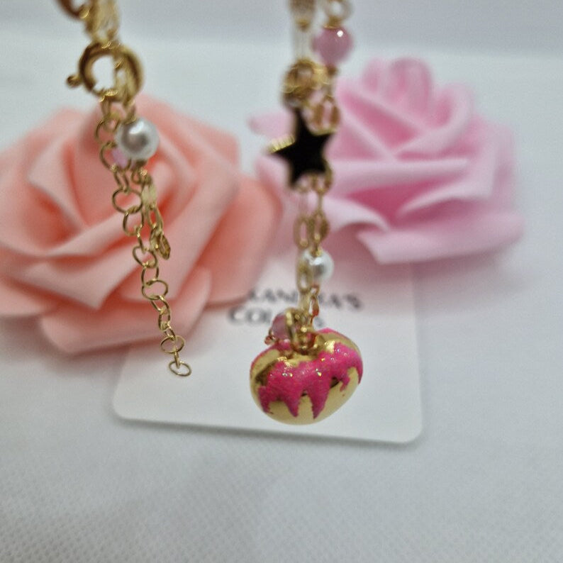 Catena dorata con perle e ciondoli, inclusa una ciambella rosa, su sfondo di rose.