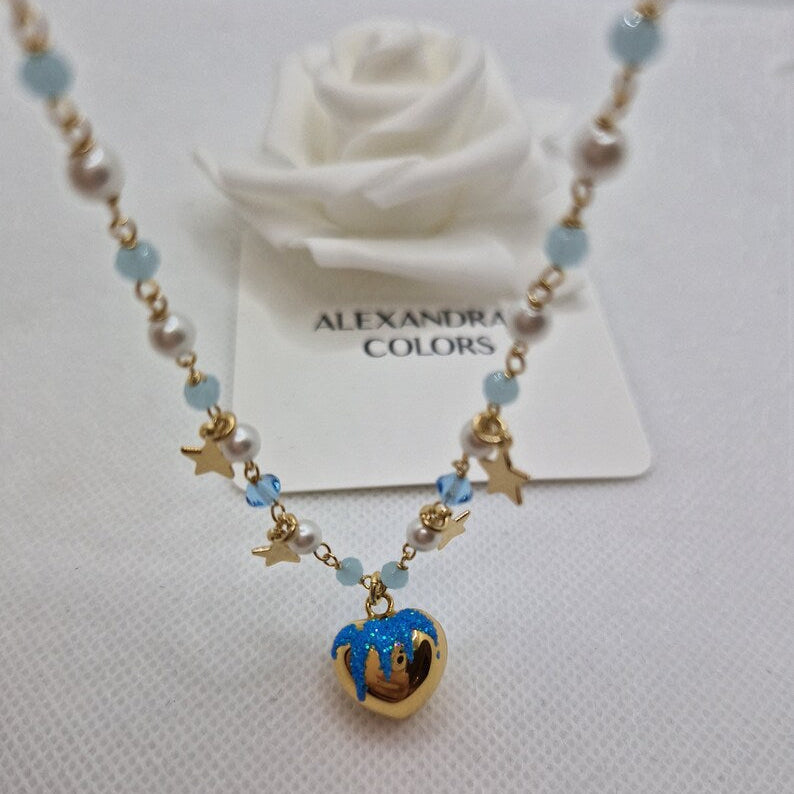 Collana con perle e cuori, con ciondolo a forma di cuore smaltato in blu e oro, su sfondo bianco.