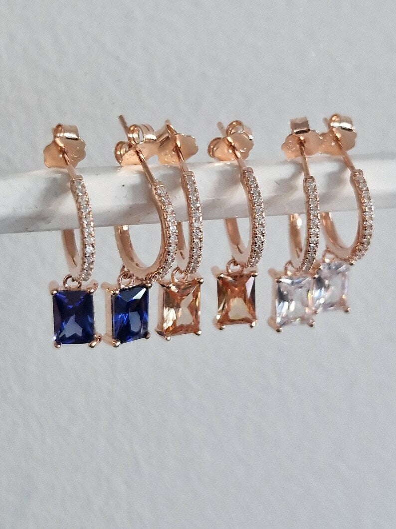 Orecchini pendenti in oro rosa con cerchio tempestato di zirconi e ciondoli quadrati in tre colori: blu, arancione e bianco.